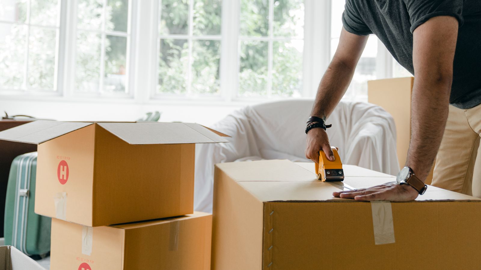 A Maven Moving crew member sealing a packed moving box with a tape gun, surrounded by stacked boxes
