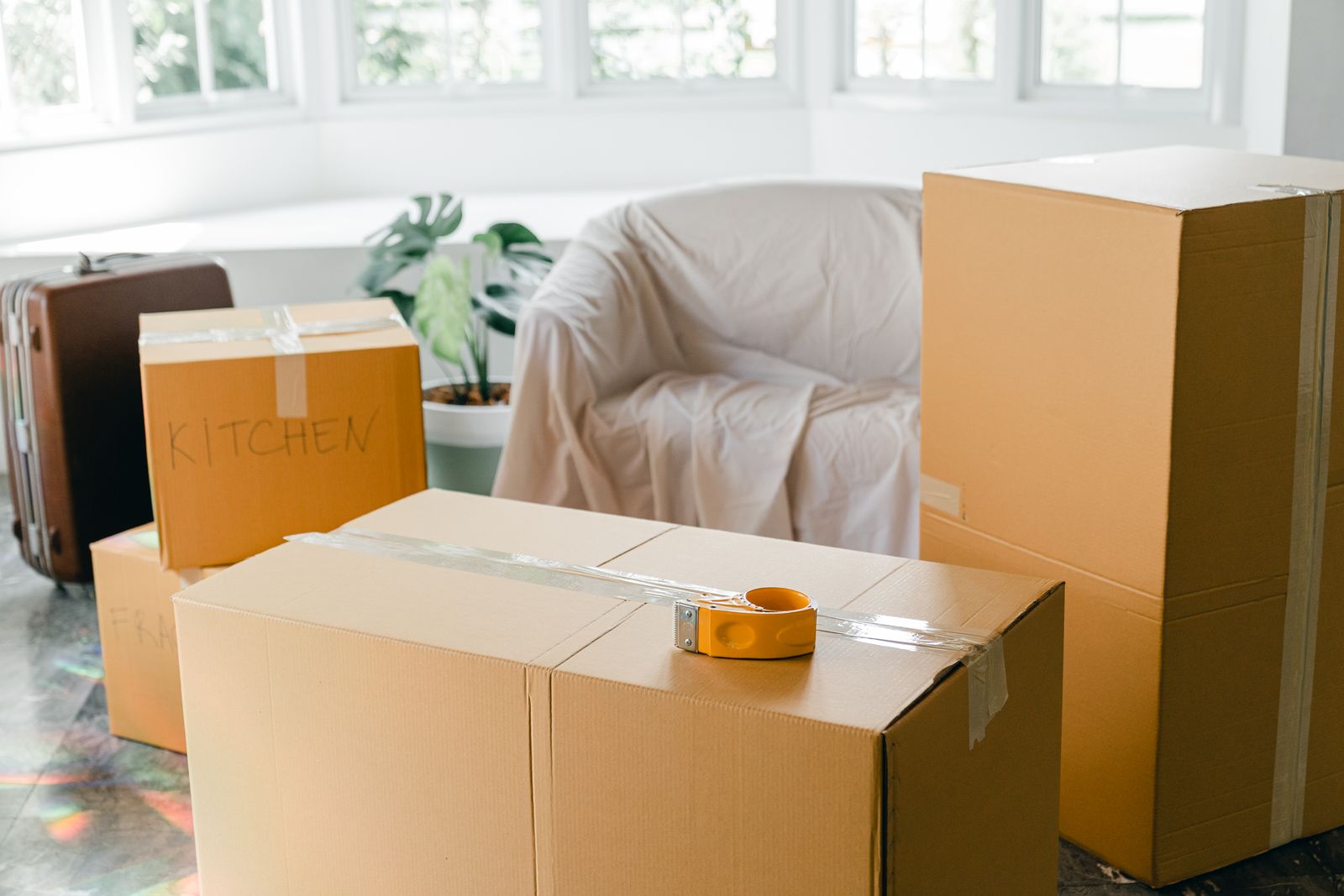 Labeled KITCHEN moving boxes sealed with a tape gun, furniture protected under a cover