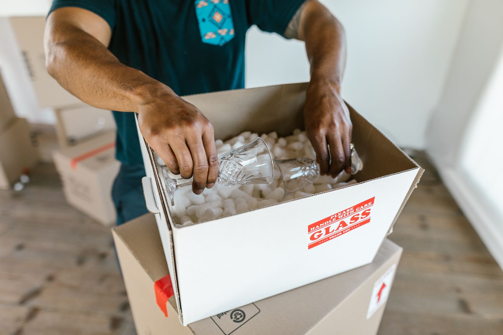 A Maven Moving crew member carefully packing fragile glassware into a HANDLE WITH CARE box